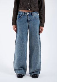 Wide-leg denim jeans in light blue, featuring a faded wash, five-pocket design, and contrasting stitching, paired with a dark cropped jacket.
