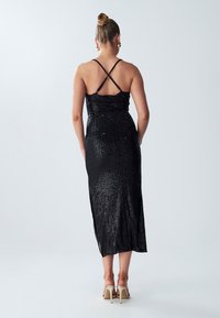 Abito midi nero in paillettes con spalline incrociate, silhouette aderente e uno spacco laterale. Texture liscia con una finitura lucente.