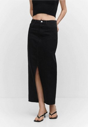 Žena nosící černou džínovou midi sukni s vysokým pasem a předním rozparkem, černý crop top a černé sandály na podpatku stojí na bílém pozadí.