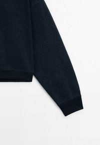 Tummansininen denim-huppari, jossa on pyöreä pääntie, resorit hihansuissa ja sileä pinta. Malli on rento ja tyyli minimalistinen.