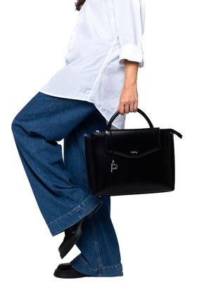 Person wearing white shirt and blue wide-leg jeans holding a black leather handbag by its top handle.