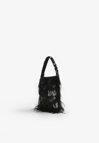 Bolso negro con un exterior texturizado de plumas, acentos circulares reflectantes y un asa decorada. Diseño compacto y vertical.
