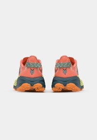 Trail running shoes with a coral upper, green accents, and a textured rubber sole featuring prominent orange lugs for traction.