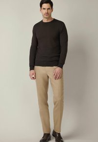 Brązowy dzianinowy sweter z długim rękawem, jasnobeżowe dopasowane spodnie i ciemne buty. Gładka tekstura, klasyczny wzór, dopasowany krój.