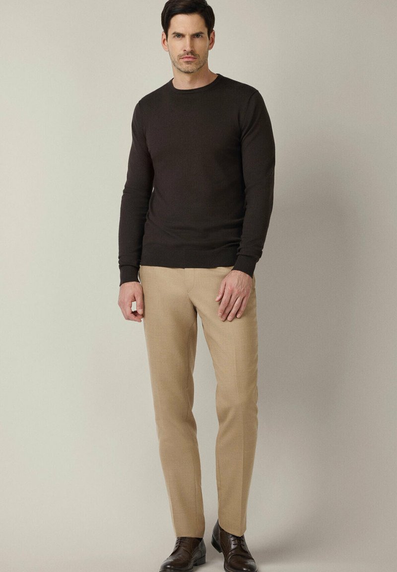 Brązowy dzianinowy sweter z długim rękawem, jasnobeżowe dopasowane spodnie i ciemne buty. Gładka tekstura, klasyczny wzór, dopasowany krój.