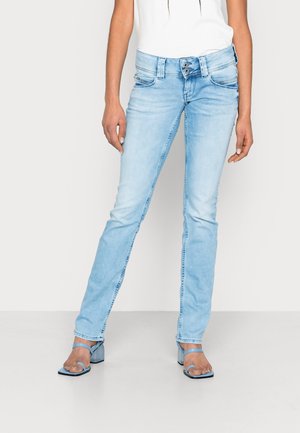 Lyseblå højttaljede skinny jeans med dobbelt knaplukning, båret med blå hælede sandaler med firkantet tå og en hvid top.