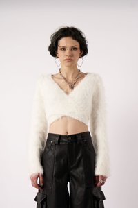 Hvit, kort fuzzy genser med v-hals og lange ermer, sammen med høyhåstede svarte lærbukser med lommer og knappelukking.