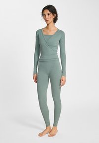 Groene tweedelige sportoutfit met een overslag langarmshirt en nauwsluitende leggings, gemaakt van een gestructureerde, rekbare stof.
