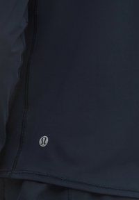 Granatowa sportowa bluzka wykonana z elastycznego materiału, charakteryzująca się gładką teksturą, przeszywanymi szwami i małą metką z logo w pobliżu dołu.