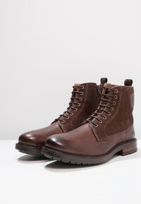 Bruna läder- och mockaboots med rund tå, snörning i fronten, gyllene öglor och en staplad sula. Har en dragflik på baksidan.