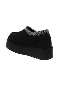 Zapato de ante negro con punta redondeada, que cuenta con un cuello texturizado de color claro cosido y una suela negra gruesa y estriada.