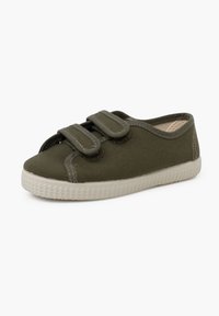 Green canvas shoe with two velcro straps, rounded toe, and textured rubber sole. Contrast stitching adds detail to the design.