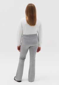 Grijze uitlopende broek met een hoge taille en een soepele textuur, gecombineerd met een witte lange mouwen trui, gezien van achteren.