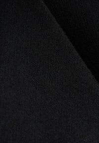 Gros plan d'un tissu noir doux avec une surface légèrement texturée et duveteuse, et des plis qui se chevauchent.