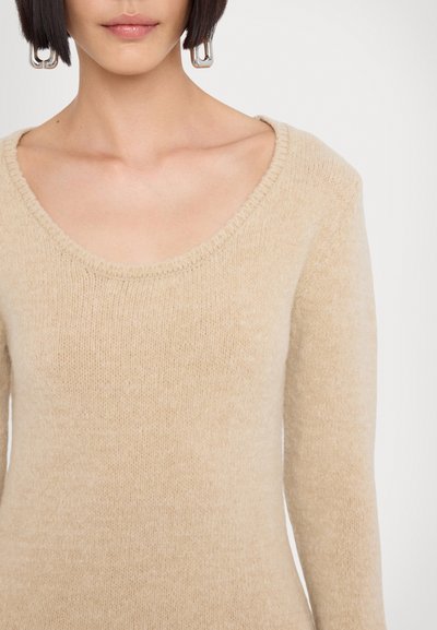 Maglione beige con scollo a barca, maniche lunghe e un morbido tessuto di maglia testurizzato. Il design è semplice ed elegante. Orecchini in metallo argentato.