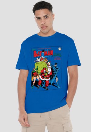 Young man wearing a blue Batman t-shirt featuring Santa Claus carrying a gift sack, flanked by Batman and Robin.
