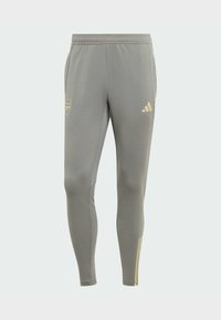 Pantalones deportivos de color gris claro con un ajuste ceñido, que cuentan con un logo dorado y detalles en dorado. Están hechos de un material suave y elástico con una cinturilla elástica.