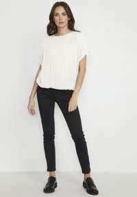 White, short-sleeve top with a relaxed fit, textured fabric, paired with black slim-fit pants and black loafers. Simple, minimal design.