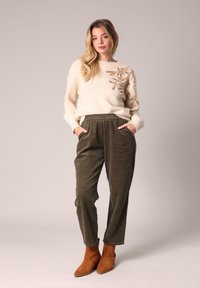 Romige trui met gouden bladeren borduurwerk, gecombineerd met olijfgroene corduroy broek en bruine suède enkellaarsjes. Zachte textuur, relaxte pasvorm.