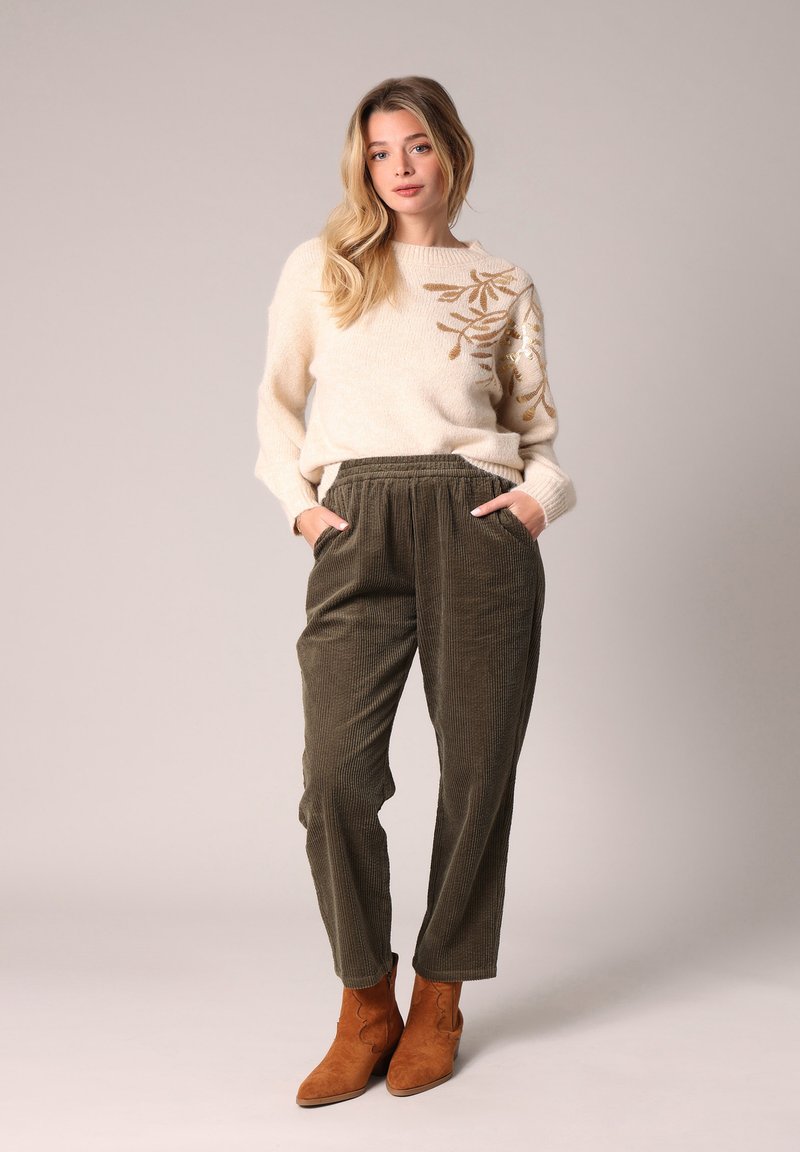 Romige trui met gouden bladeren borduurwerk, gecombineerd met olijfgroene corduroy broek en bruine suède enkellaarsjes. Zachte textuur, relaxte pasvorm.