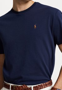 Mörkblå bomullströja med rund hals och korta ärmar, med en liten broderad logo på bröstet och en mjuk yta.