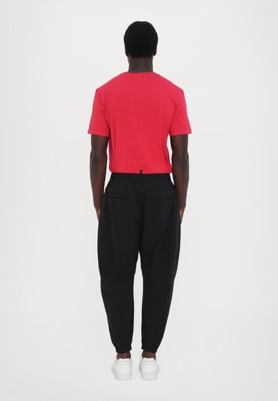 Red short-sleeve t-shirt with a round neck, paired with black tapered pants featuring elastic cuffs and side pockets. White sneakers complete the look.