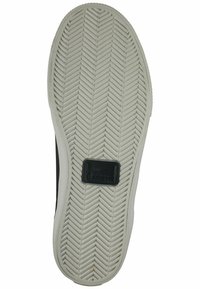 Rubber shoe sole featuring a herringbone pattern, predominantly white with black accents, and a rectangular Lacoste logo tag near the heel.