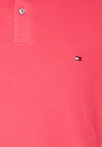 Polo in un vivace corallo, con tessuto strutturato, patta con tre bottoni e un piccolo logo con dettagli rossi, bianchi e blu.