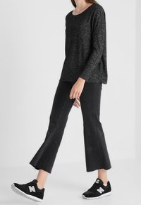 Svart stickad långärmad topp, något oversized, kombinerad med cropped svarta utsvängda jeans och svarta sneakers med vita detaljer.