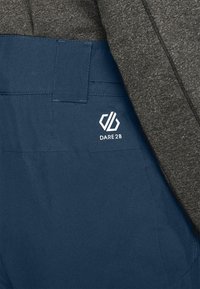 Marineblaue Hose mit glatter Textur, ausgestattet mit einer Gesäßtasche und einem weißen "DARE2B"-Logo am Bund. Darüber ist grauer Stoff sichtbar.