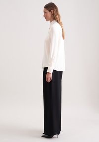 White long-sleeve blouse with a collar, smooth texture, and buttoned cuffs, paired with high-waisted black trousers, and pointed black heels.