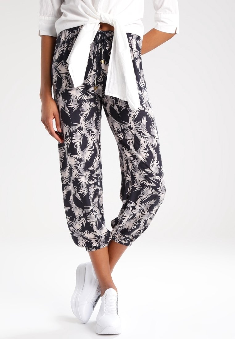 Pantalones con estampado en blanco y negro con diseño de hojas de palma, con cinturilla elástica y tobillos puñados, combinados con zapatillas blancas.
