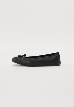 Black flat ballet shoe with rubber sole and small bow on toe, shown from side on plain white background.