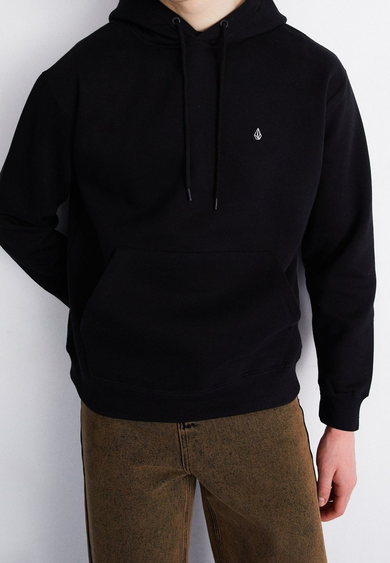 Zwarte hoodie met een voorzak, verstelbare trekkoorden in de capuchon en een klein logo op de borst. Het materiaal lijkt zacht en warm.