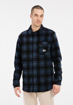 Camisa de franela a cuadros en negro y azul con cierre de botones en el frente, cuello puntiagudo y un bolsillo de parche con un logo en el lado izquierdo del pecho.
