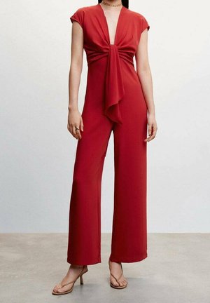 Czerwony kombinezon z głębokim dekoltem w serek i wiązaniem z przodu. Krótkie rękawy typu cap i szerokie nogawki. Gładka tkanina, styl minimalistyczny, zestawiony z sandałami.