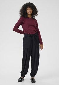 T-shirt bordeaux à manches longues associé à un pantalon noir ample avec taille élastique et larges poignets ; tissu doux et deux poches.