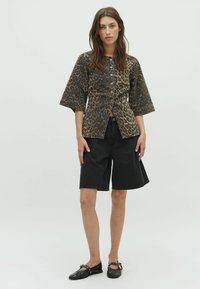 Leopardenmuster Kurzarmjacke mit Knopfverschluss, kombiniert mit schwarzen Denim-Shorts. Schwarze flache Schuhe runden das Outfit ab.