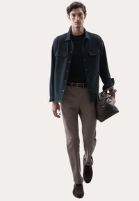 Camisa de botones azul oscura sobre una blusa negra, pantalones beiges y mocasines marrones, sosteniendo una bolsa marrón, diseño minimalista, textura suave.