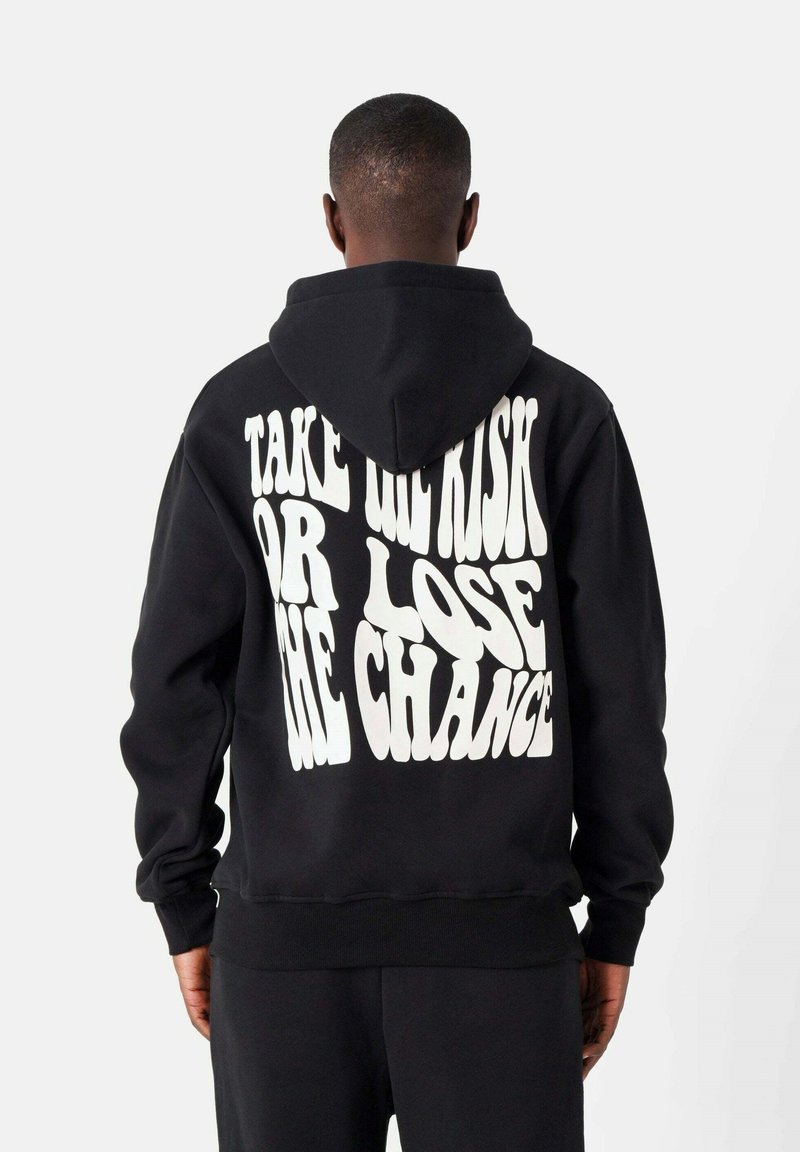 Sudadera negra de algodón con un bolsillo frontal. Presenta un gran texto gráfico en blanco en la parte posterior: "NO CORRAS RIESGOS O PIERDE LA OPORTUNIDAD."