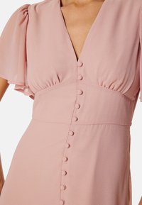 Robe enroulée rose avec des manches courtes et légères, décolleté en V profond et une ligne de boutons ronds sur le devant. Tissu doux et léger.