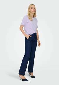 Lyse lilla kortærmet skjorte parret med mørkeblå høj talje denimbukser. Skoene er sorte hælede mules med en spidse tå design.