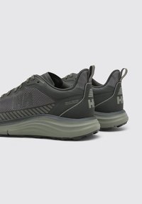 Chaussures de sport vert foncé avec une tige en mesh texturé, des accents en caoutchouc contrastants et une semelle amortissante. Détail du logo sur le talon.
