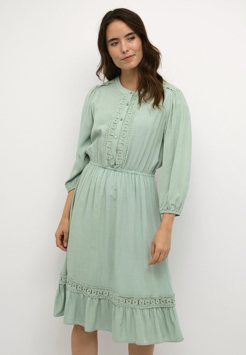 Mint green dress with long puff sleeves, lace detailing along the bodice, and a ruffled hem. Soft fabric with an elastic waist.