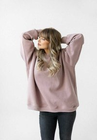 Przesadna różowa bluza z opadającymi ramionami, ściągaczami na rękawach i u dołu, zestawiona z czarnymi dżinsami. Gładka tekstura i luźny krój.