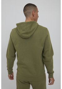 Felpa con cappuccio verde oliva realizzata in cotone morbido. Presenta polsini e orlo a costine, con una vestibilità rilassata e senza modelli o marchi in vista.
