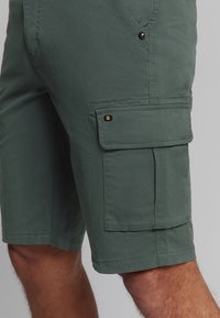 Heren cargoshorts in donker groen, gemaakt van lichtgewicht stof met zijzakken en drukknoopdetails. Heeft een ontspannen pasvorm en gestikte naden.