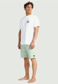 T-shirt branca com um gráfico colorido no peito, combinada com calções verdes claros feitos de tecido texturizado, com um detalhe de logótipo.