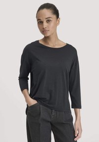 Schwarz langärmliges Oberteil aus weichem Stoff, mit weitem Ausschnitt und lässiger Passform, kombiniert mit hoch taillierten dunklen Denim-Hosen.