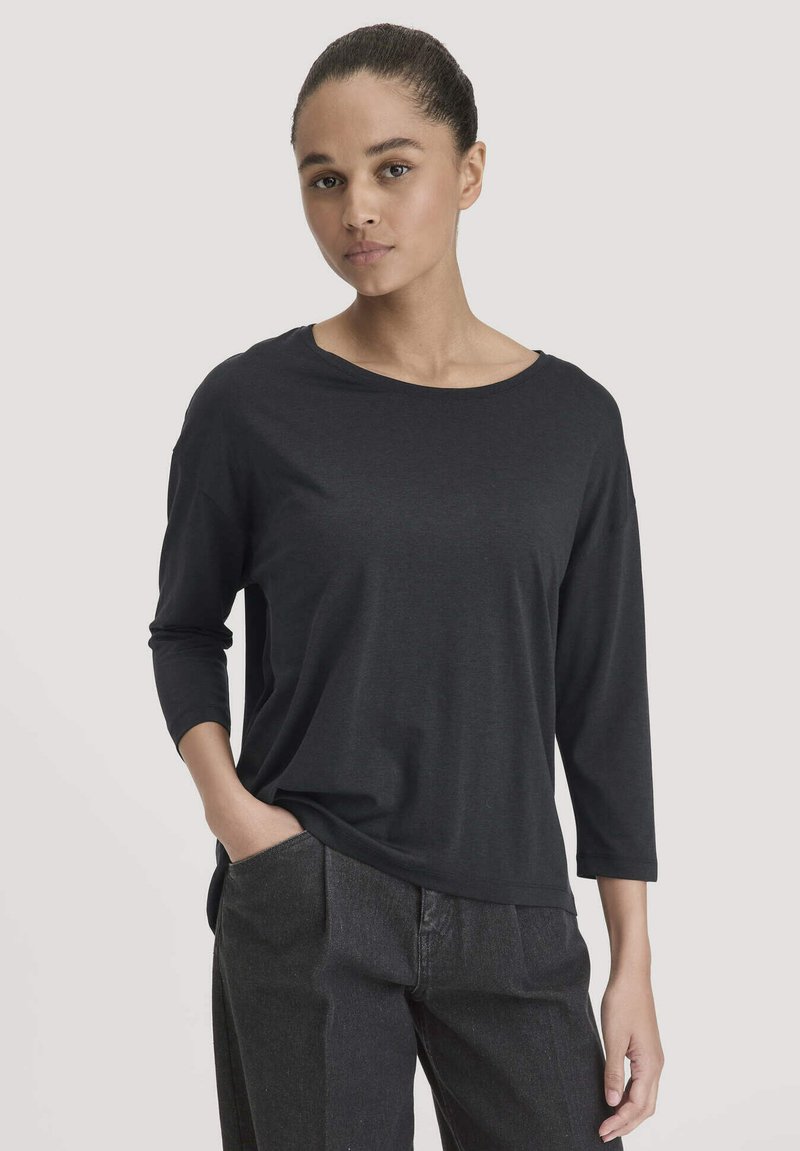 Schwarz langärmliges Oberteil aus weichem Stoff, mit weitem Ausschnitt und lässiger Passform, kombiniert mit hoch taillierten dunklen Denim-Hosen.